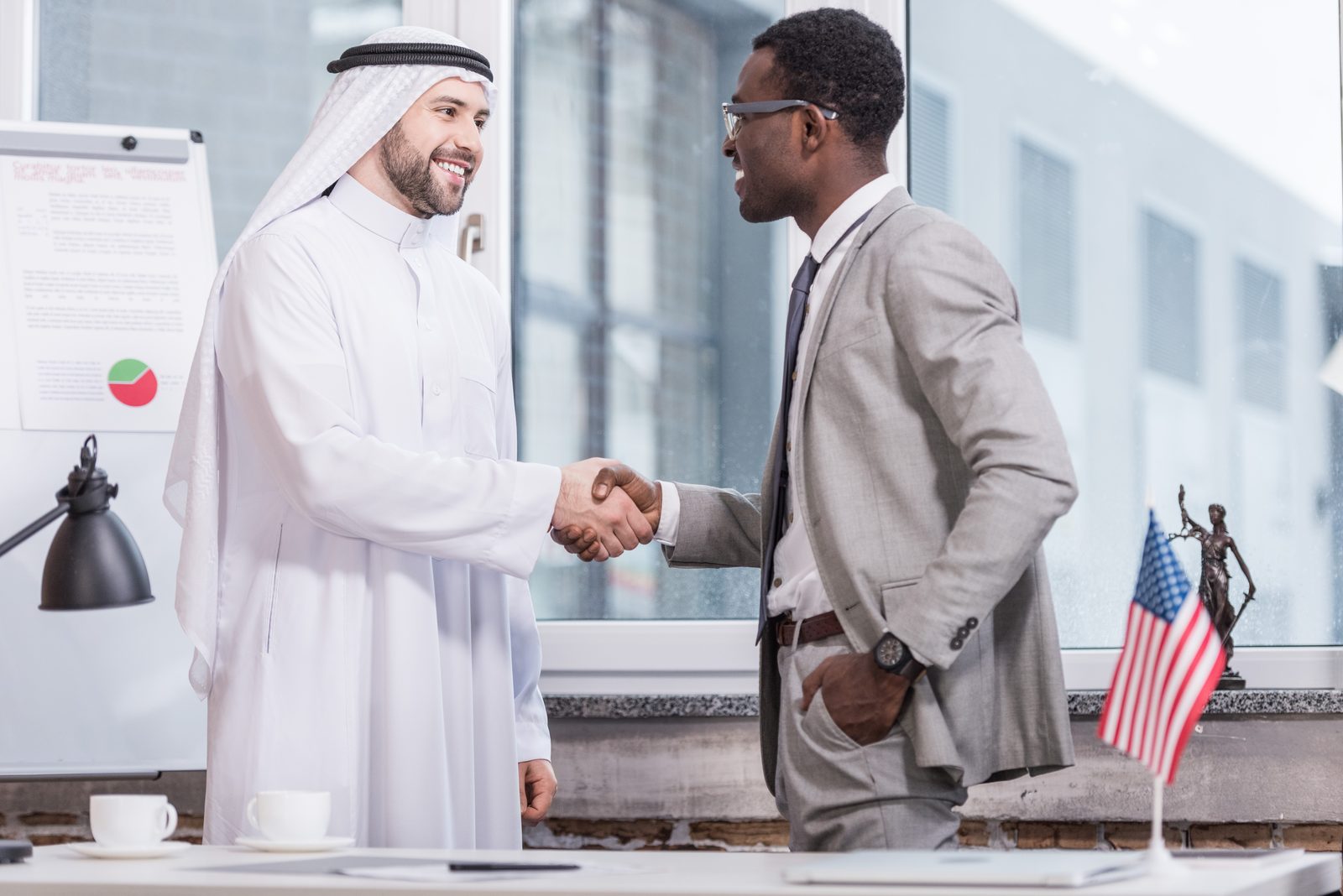 Trader in Emirati dress shaking hands with a buyer in an office